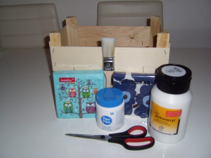 Holzkiste, Servietten, Pinsel, Kleber, Schere und Dekoracryl auf Tisch; reinigung möglich.